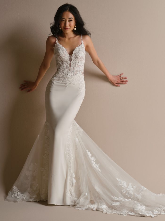Bride wearing an ivory fit-and-flare wedding dress with a plunging V-neckline, floral lace bodice, delicate straps, and lace-trimmed train.