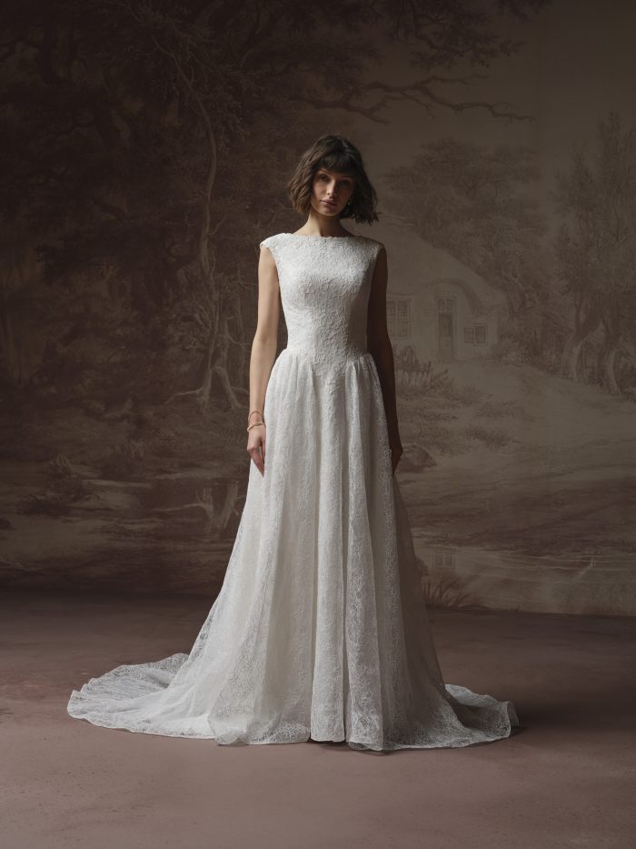 Bride wearing an ivory lace A-line wedding dress with a bateau neckline, cap sleeves, fitted waist, and flowing skirt with a soft train.