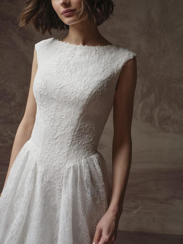 Close-up of an ivory lace wedding dress featuring a bateau neckline, cap sleeves, fitted bodice, and delicate floral lace.