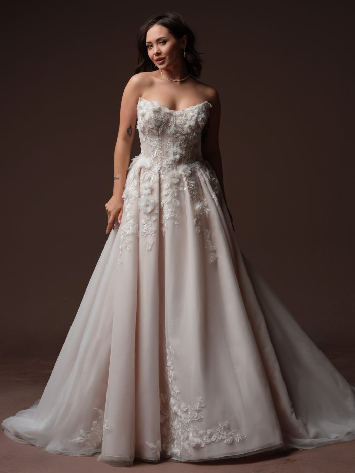 Bride wearing the Rebecca Ingram Fleur ballgown wedding dress with a strapless cat eye neckline, corset bodice, dimensional floral appliqués, and full skirt.