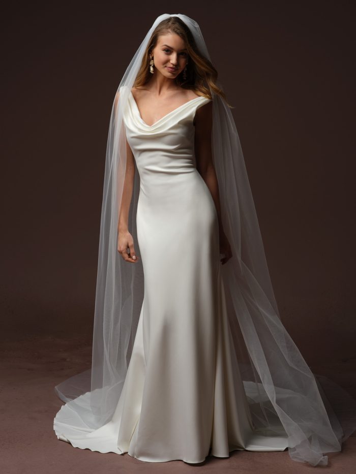 Full-length view of the Rebecca Ingram Tiana sheath wedding dress featuring a soft scoop neckline, draped satin bodice, sleek silhouette, and chapel-length veil.