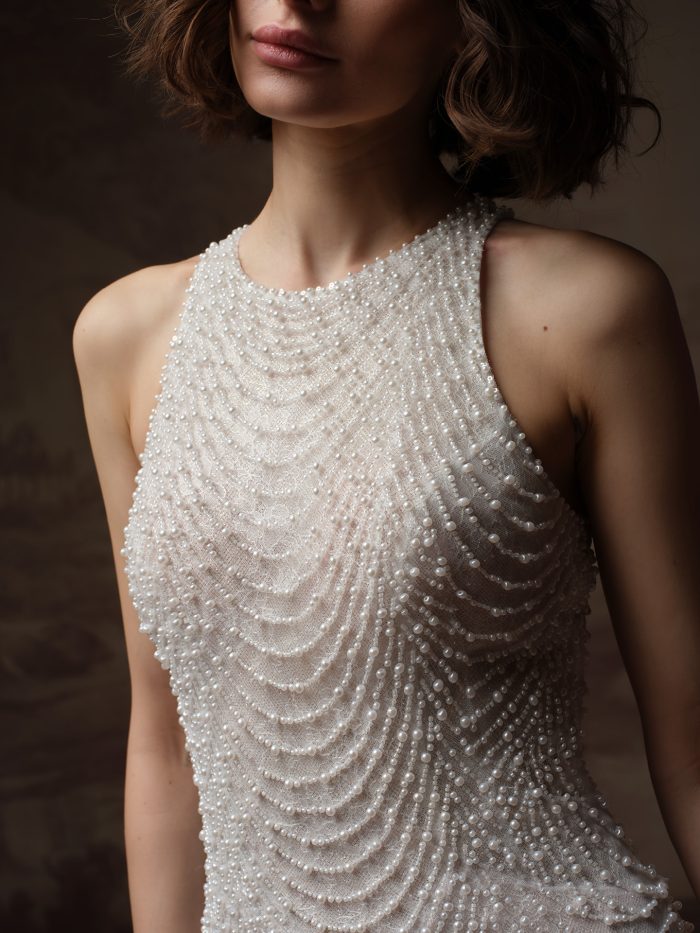 Close-up of an ivory wedding dress with a high neckline and intricate draped pearl beading across the bodice.