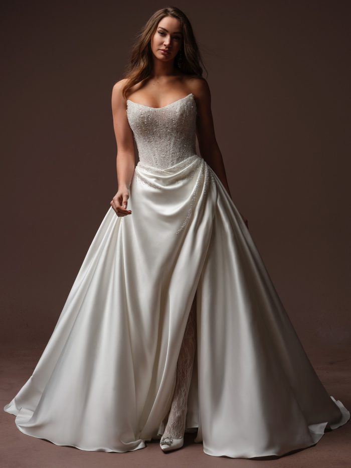 Bride wearing the Sottero and Midgley Rumi ballgown wedding dress with a strapless cat eye neckline, beaded bodice, and draped satin skirt.
