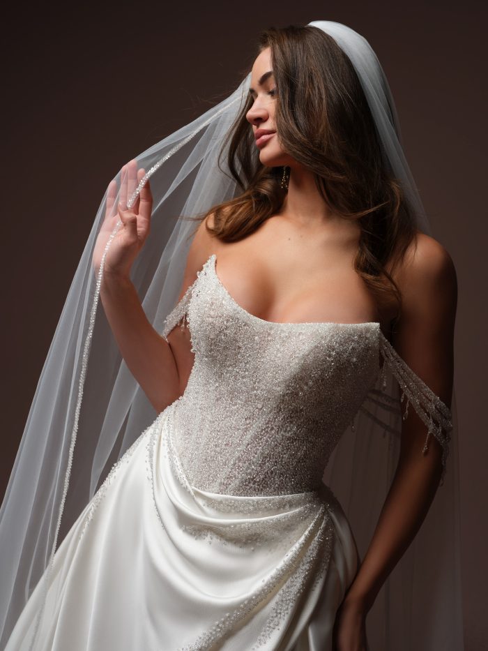 Close-up of the Sottero and Midgley Rumi ballgown wedding dress featuring a strapless cat eye neckline, beaded bodice, draped satin skirt, and beaded shoulder details.