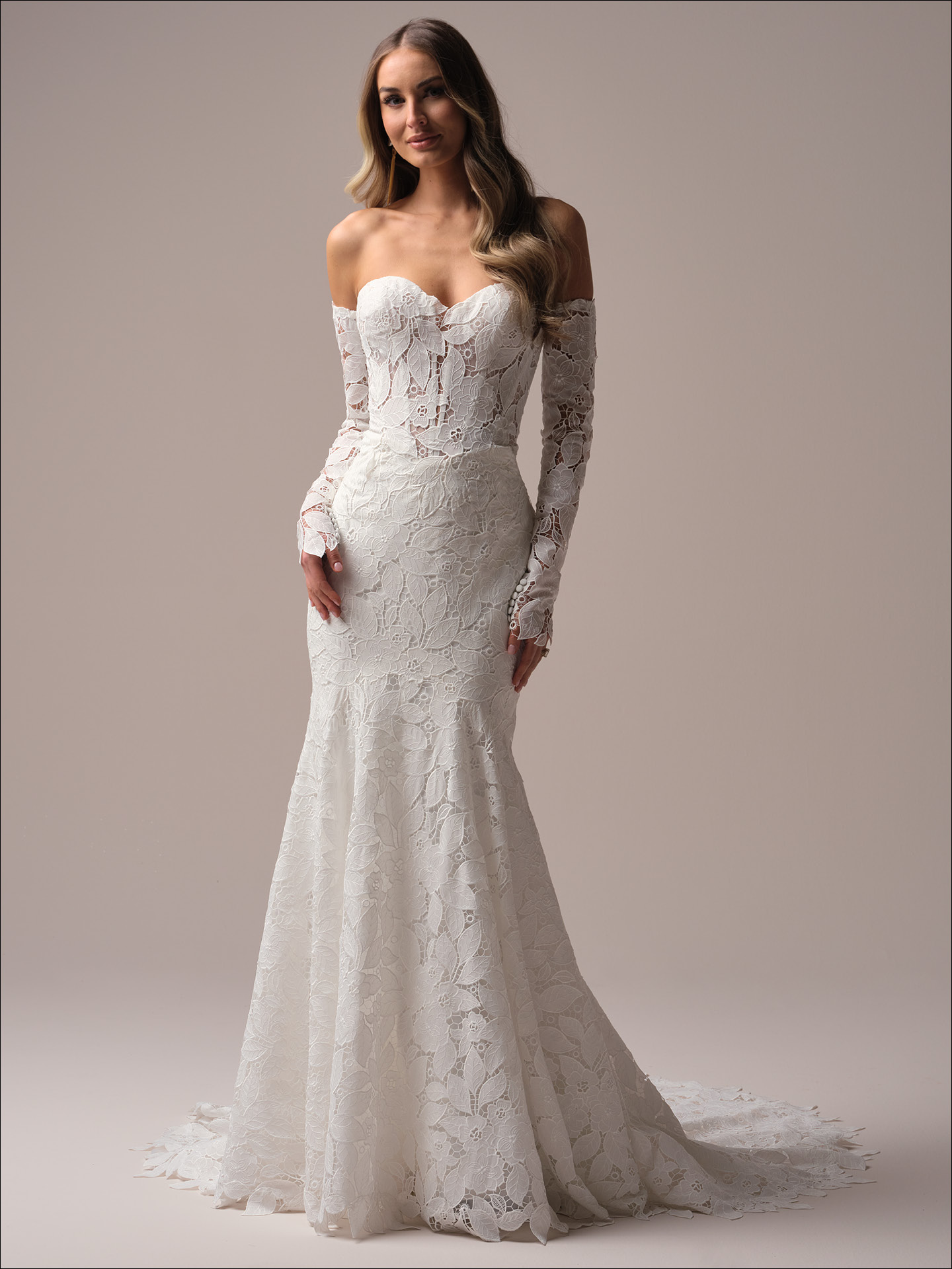 Bride wearing Dakota by Maggie Sottero, a fit-and-flare allover lace wedding dress with off-the-shoulder long sleeves, sweetheart neckline, and scalloped lace train.