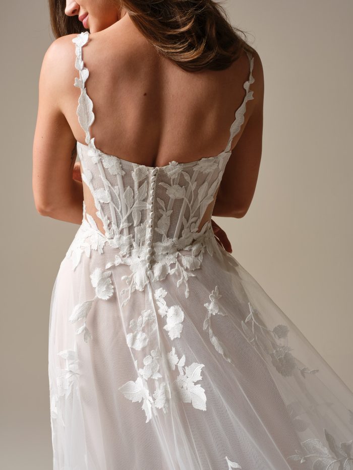 Back detail of Natalie Marie by Maggie Sottero featuring sheer lace bodice with floral appliqué, covered button closure, and delicate lace straps on an A-line wedding dress.
