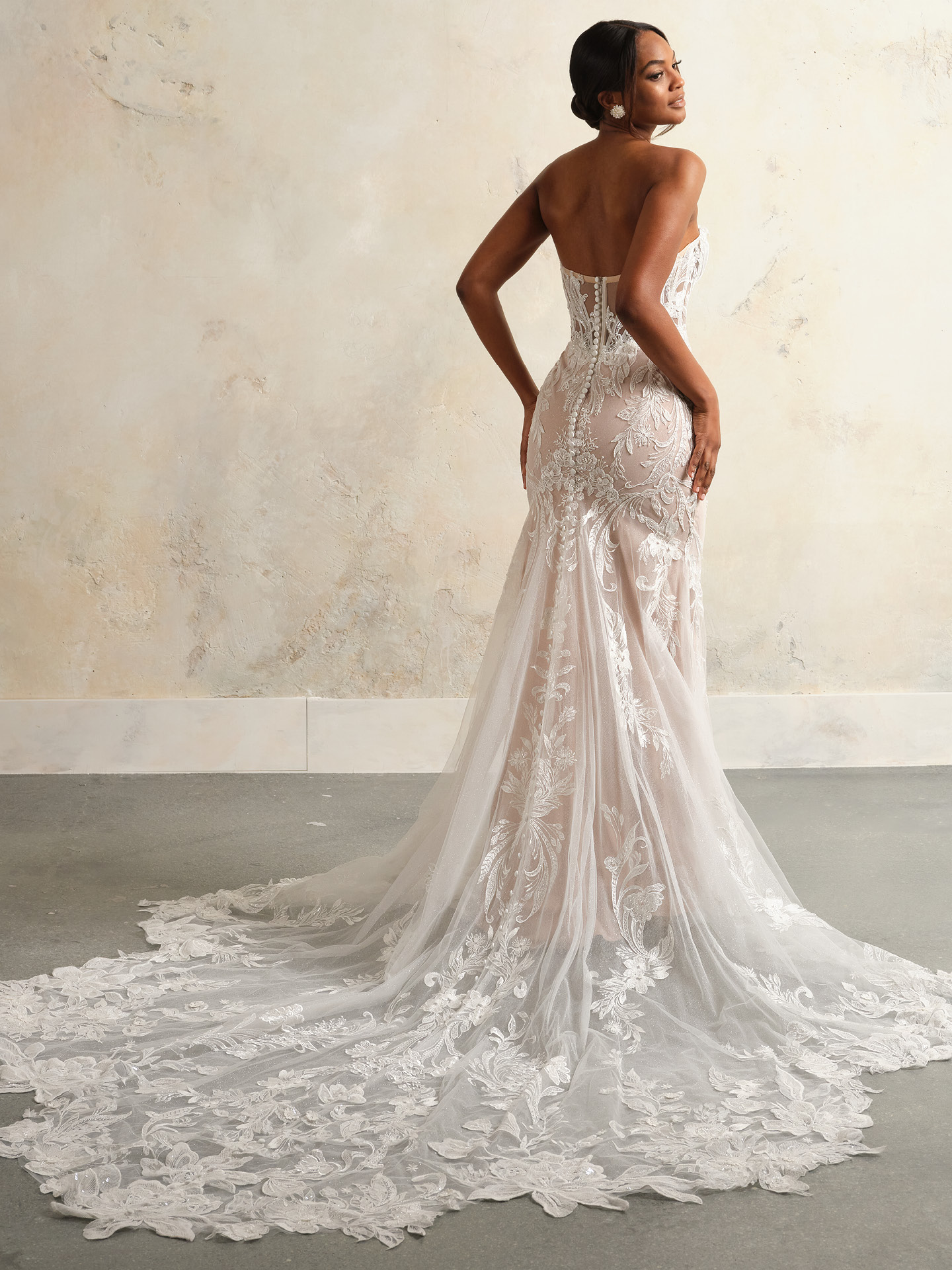 Back view of Nyjah by Sottero and Midgley featuring sheer lace bodice, covered button closure, fitted silhouette, and extended illusion lace train with floral appliqué.