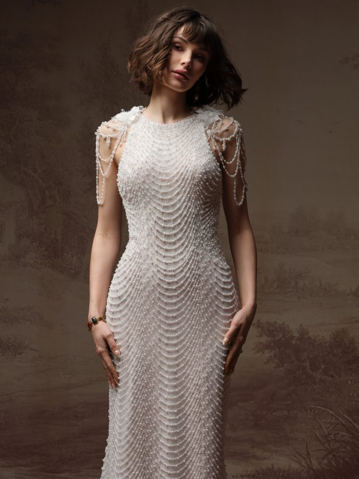 Close-up of the Oleta wedding dress with cap sleeves, featuring a high jewel neckline, an intricately beaded pearl bodice in a scalloped drape pattern, and pearl-draped cap sleeve straps with floral accents at the shoulders.