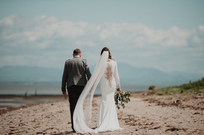 Bride Holding Grooms Hand from Back Wearing Long Sleeve Wedding Dress Aston by Sottero and Midgley 