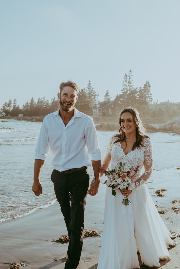 Bride Walking on Beach with Husband in Lorraine Dawn by Rebecca Ingram