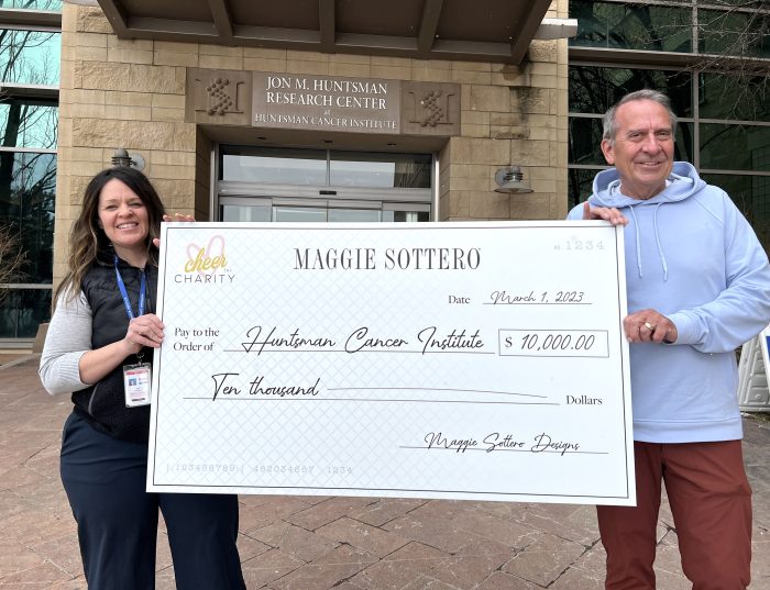 Clyde holding a check from Maggie Sottero to Huntsman Cancer Institute for $10,000 that was raised through Cheer for Charity, which is impactful for cancer research.