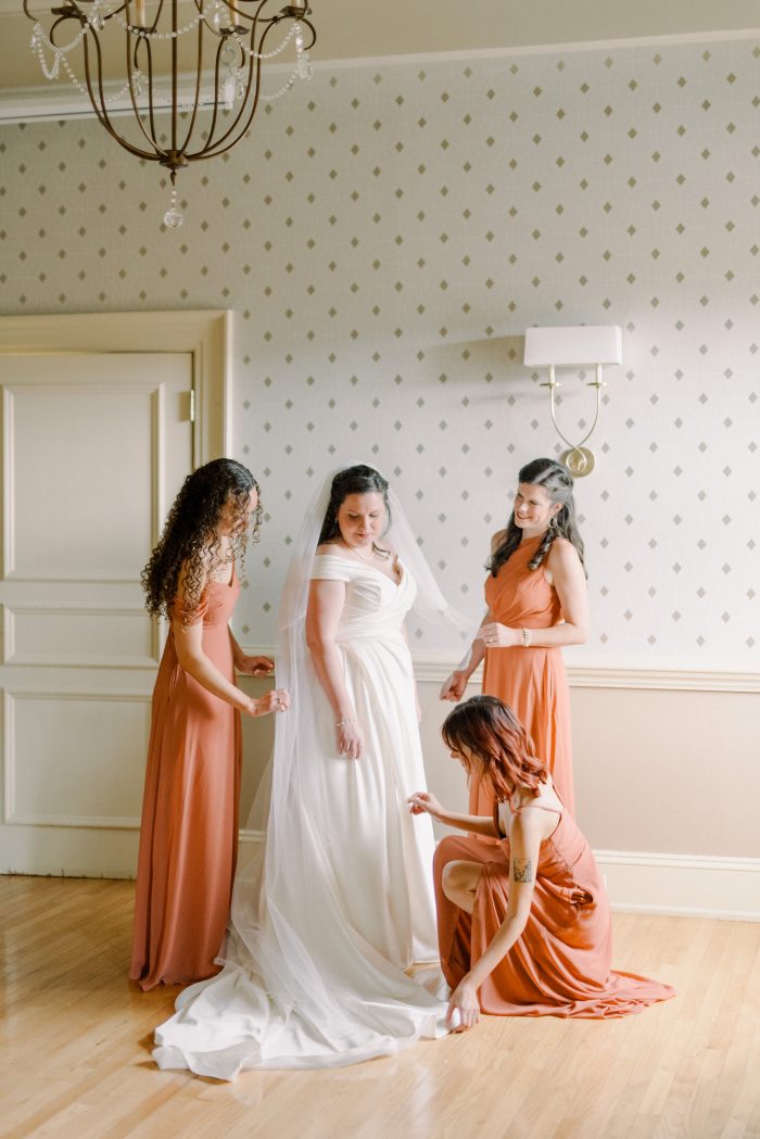 Bride wearing Ekaterina wedding dress by Maggie Sottero surrounded by her bridesmaids wearing Peach Fuzz.