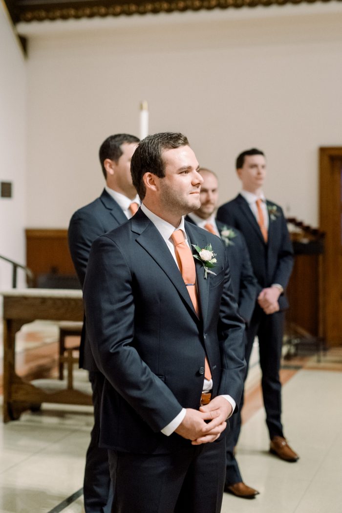 Groom standing at the end of the aisle in a peach fuzz tie.