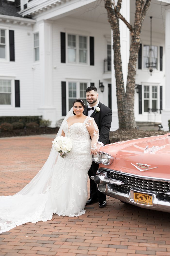 Bride wearing Fiona wedding dress by Maggie Sottero with her husband in front of a peach fuzz-colored car.