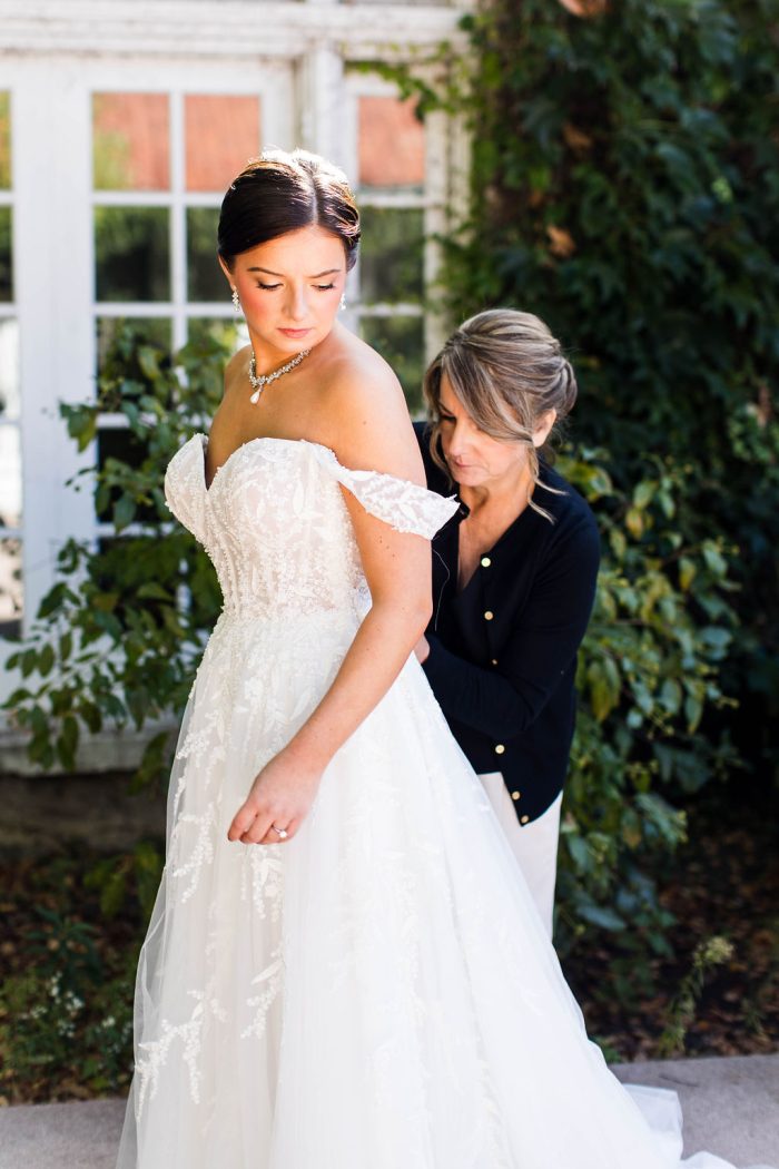 Bride wearing Oriana by Maggie Sottero while she gets buttoned up by her mother