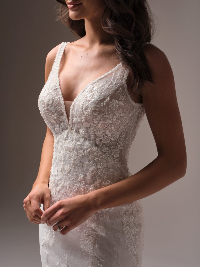 Close-up of the Eloise fit-and-flare wedding dress showing the deep V-neckline, beaded floral lace bodice, and delicate illusion straps with dimensional lace detailing.