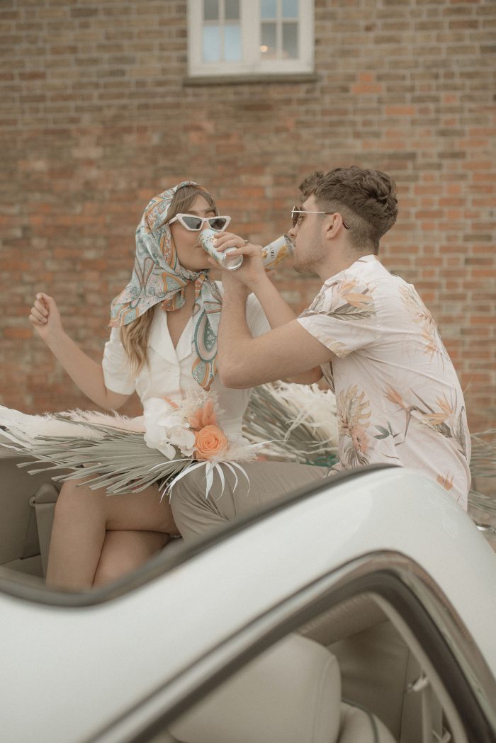 Bride and groom drinking in their retro wedding getaway car