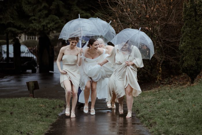 Bride wearing Scarlet by Maggie Sottero with her bridesmaids running through the rain at her outdoor wedding