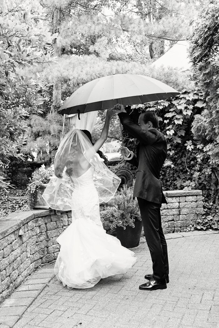 Bride wearing Hattie by Rebecca Ingram dancing in the rain with her husband at their outdoor wedding