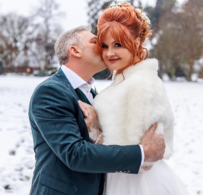 Bride wearing Joanne by Rebecca Ingram being kissed by her husband in the snow at their outdoor wedding