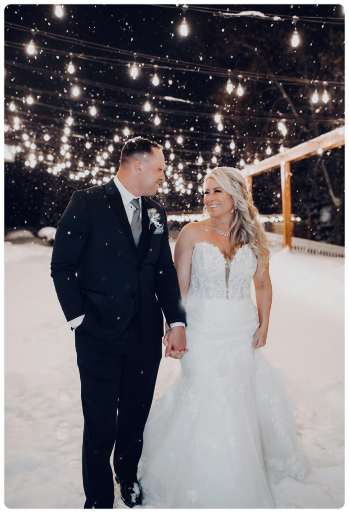 Bride wearing Lennon by Maggie Sottero holding hands with her husband in the snow at their outdoor wedding