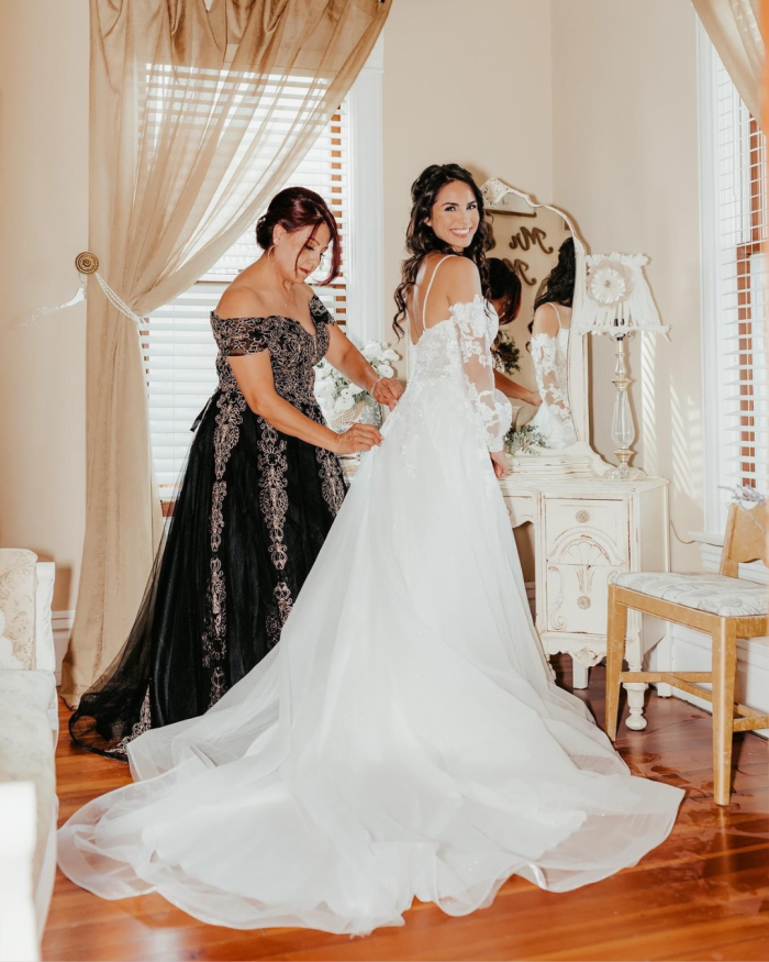 Bride wearing Stevie long sleeve wedding dress by Maggie Sottero being laced up by her mom