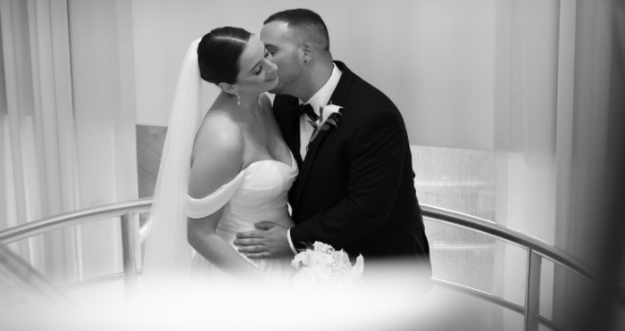 Bride wearing an off-the-shoulder wedding dress by Maggie Sottero being kissed by her husband