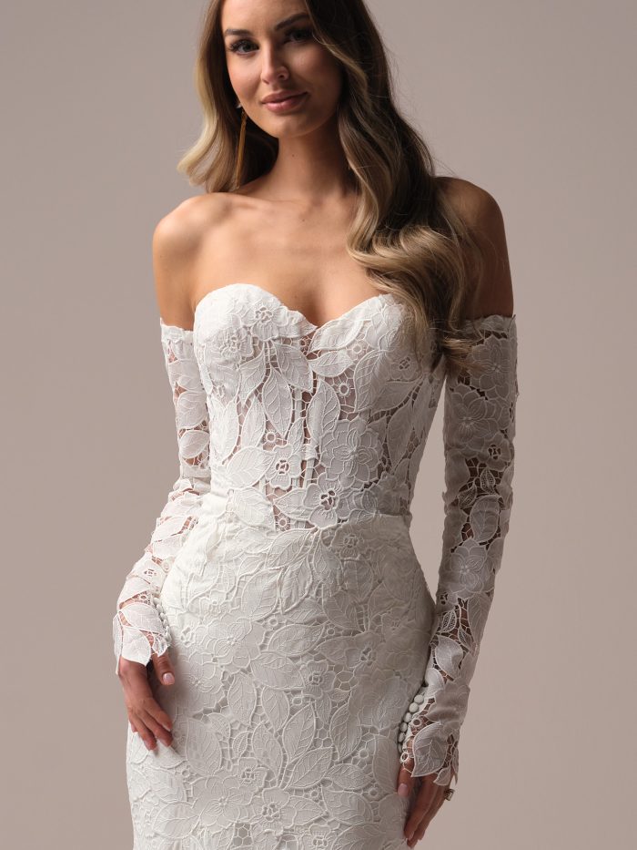 Fitted lace wedding dress with detachable off-the-shoulder long sleeves, designed with bold floral lace motifs and button cuff accents.