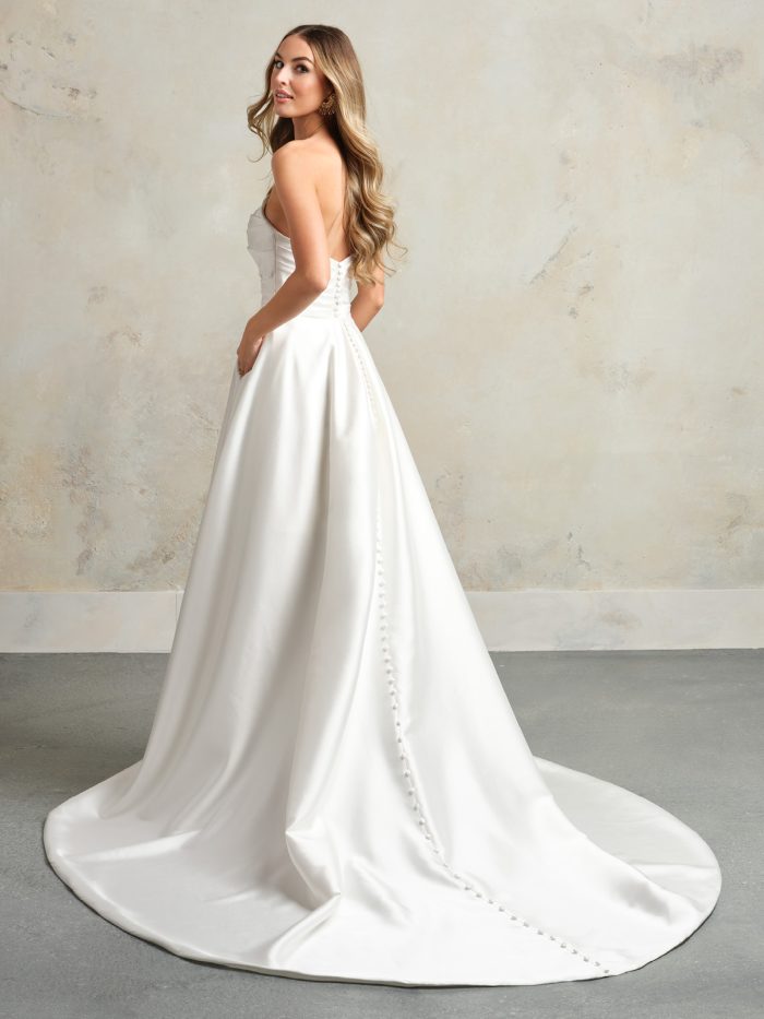Classic strapless satin wedding dress with a clean A-line silhouette, detachable overskirt, and button detail trailing down the back.