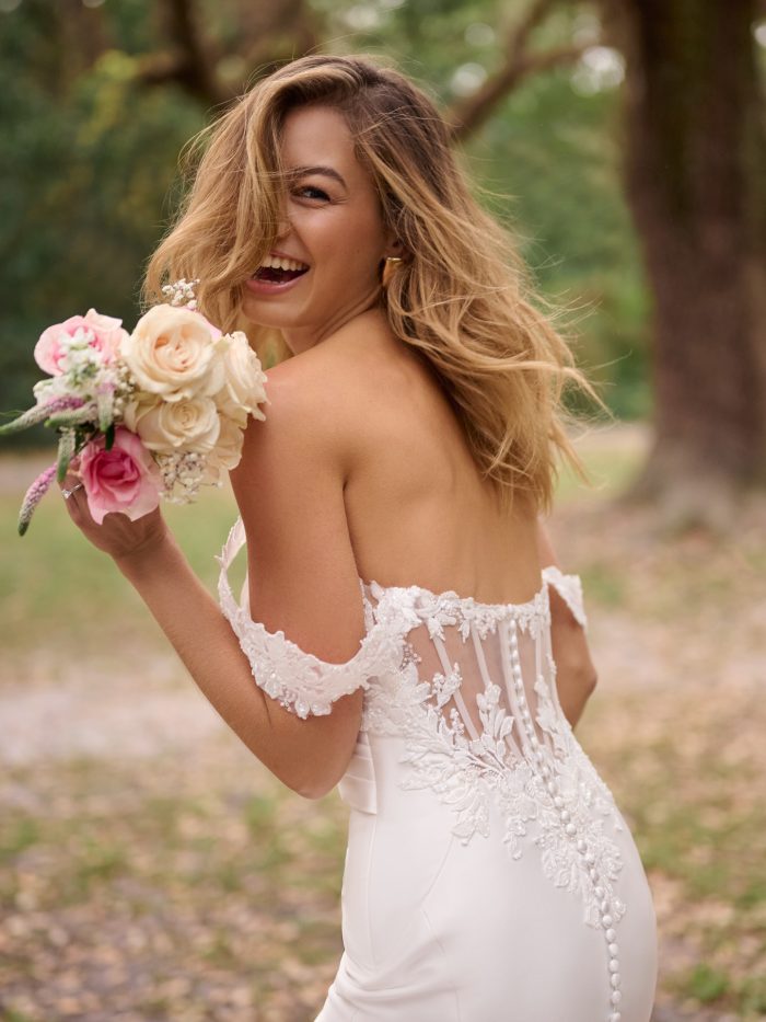 Bride wearing a sexy wedding gown with exposed boning in the back and floral details holding a bridal bouquet