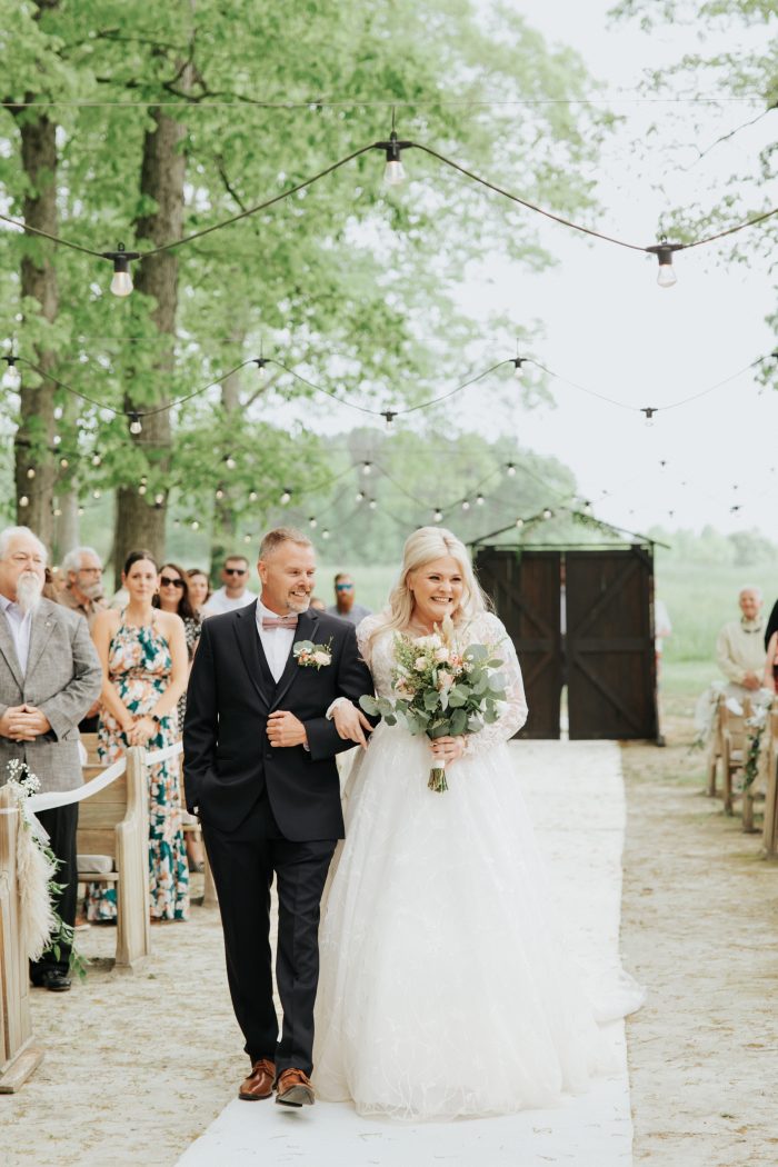 Brittany wearing one of Maggie Sottero's maternity wedding dresses walking down the aisle with her father