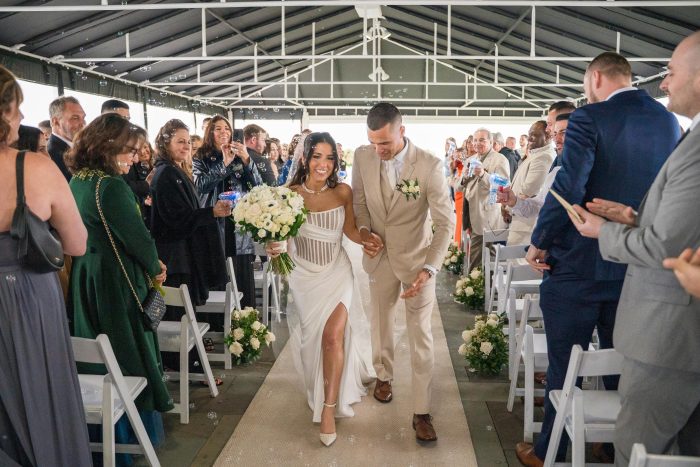 Bride wearing Gabrielle by Maggie Sottero wedding dress walks down the aisle with her partner after the ceremony as guests celebrate