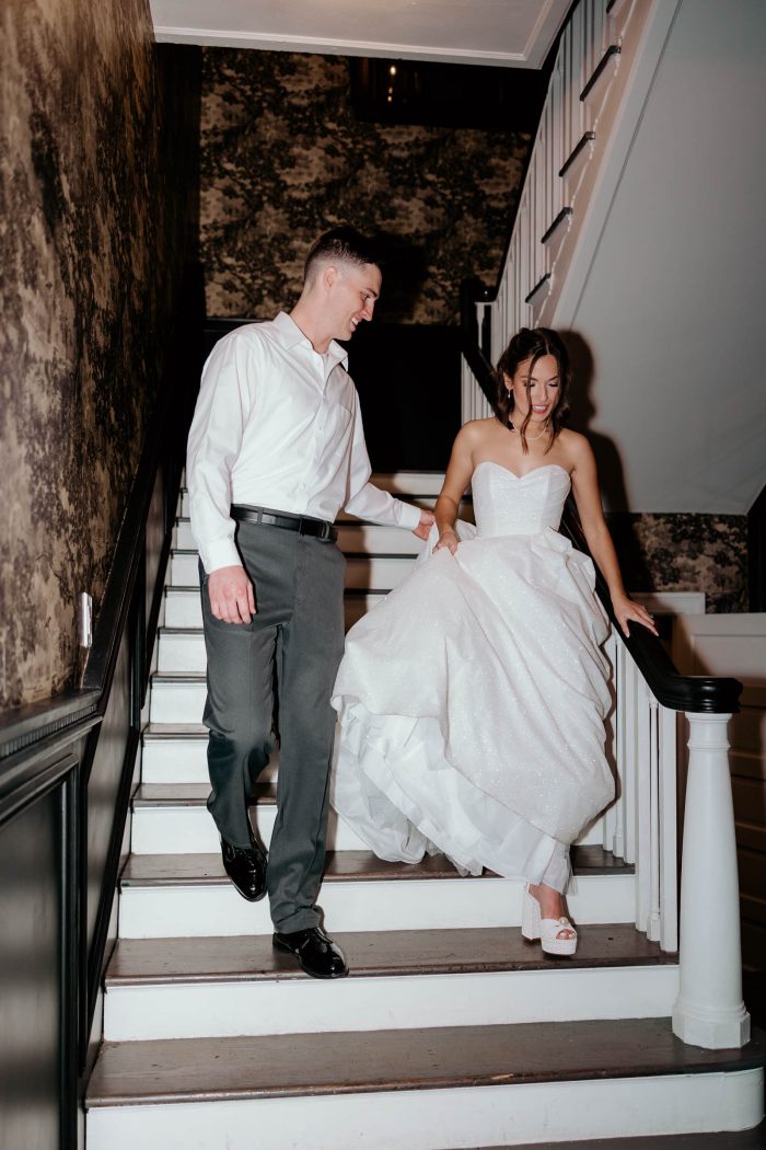 Bride wearing Anniston by Maggie Sottero in her wedding inspo pictures walking down the stairs with her husband