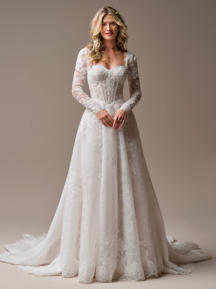 Long sleeve lace A-line wedding dress with a sheer corset bodice, sweetheart neckline, and soft floral appliqués flowing into a romantic lace train.