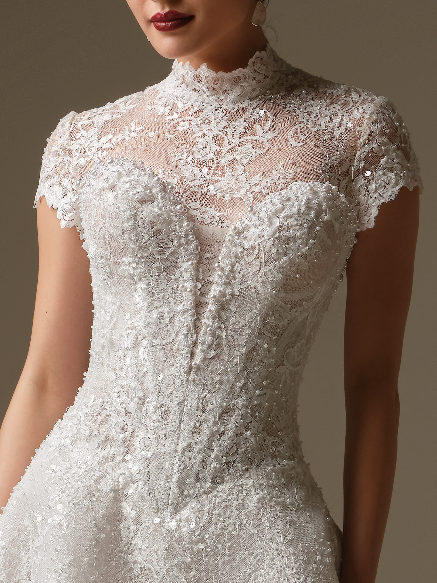 Fitted wedding gown styled with a delicate lace overlay jacket featuring a scalloped high neck and intricate beading for added coverage and texture.