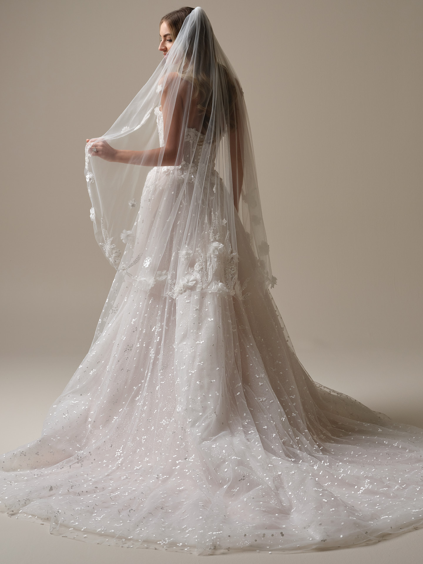 Fingertip-length veil in soft sheer tulle with delicate floral appliqué and subtle shimmer, falling gracefully to the bride’s fingertips for a romantic, lightweight finish.