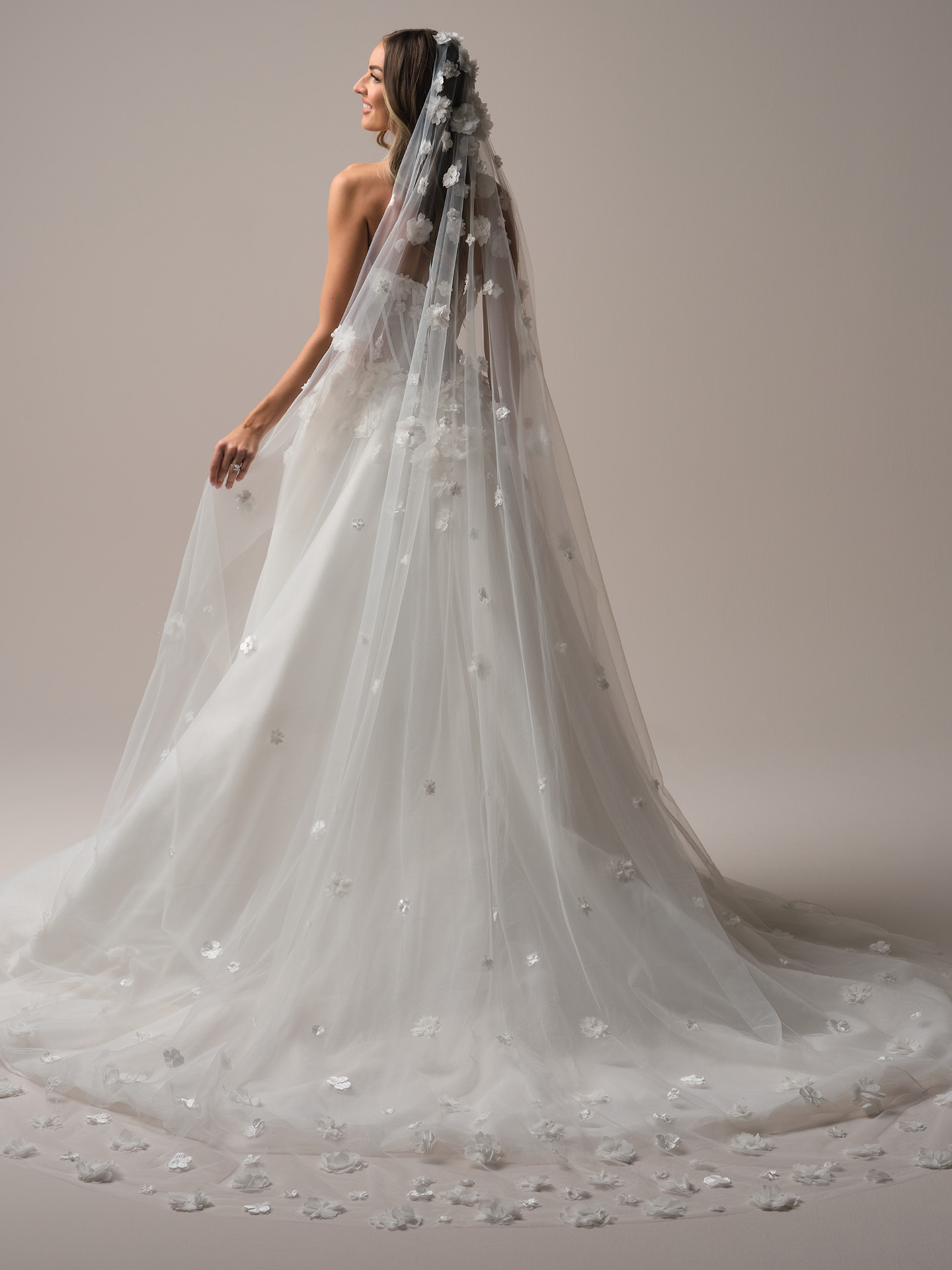 Chapel-length tulle veil adorned with scattered 3D floral appliqué, creating soft dimension and a romantic trailing effect.