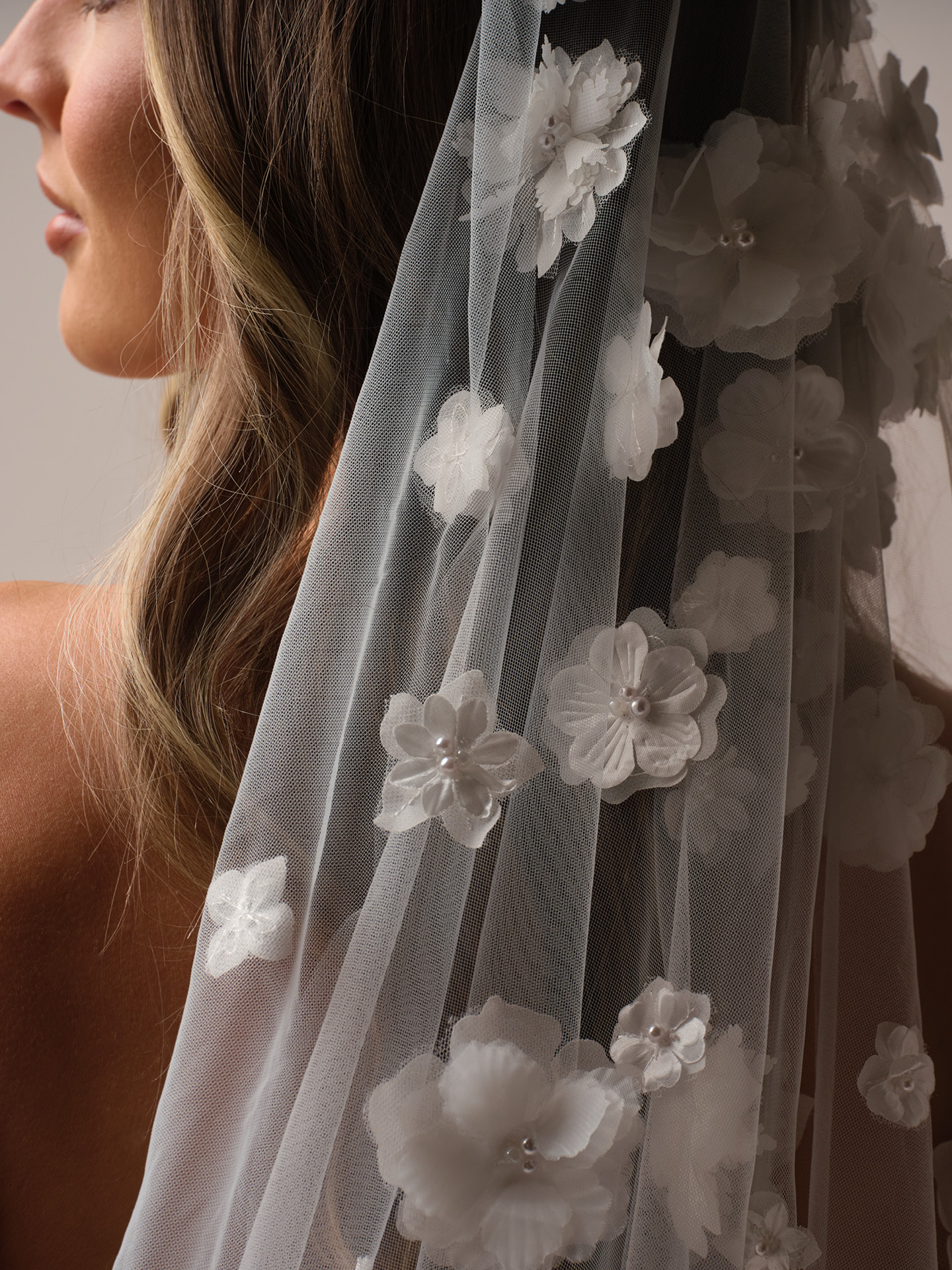 Close-up of a chapel-length veil featuring delicate 3D floral appliqué with subtle pearl accents on sheer tulle.