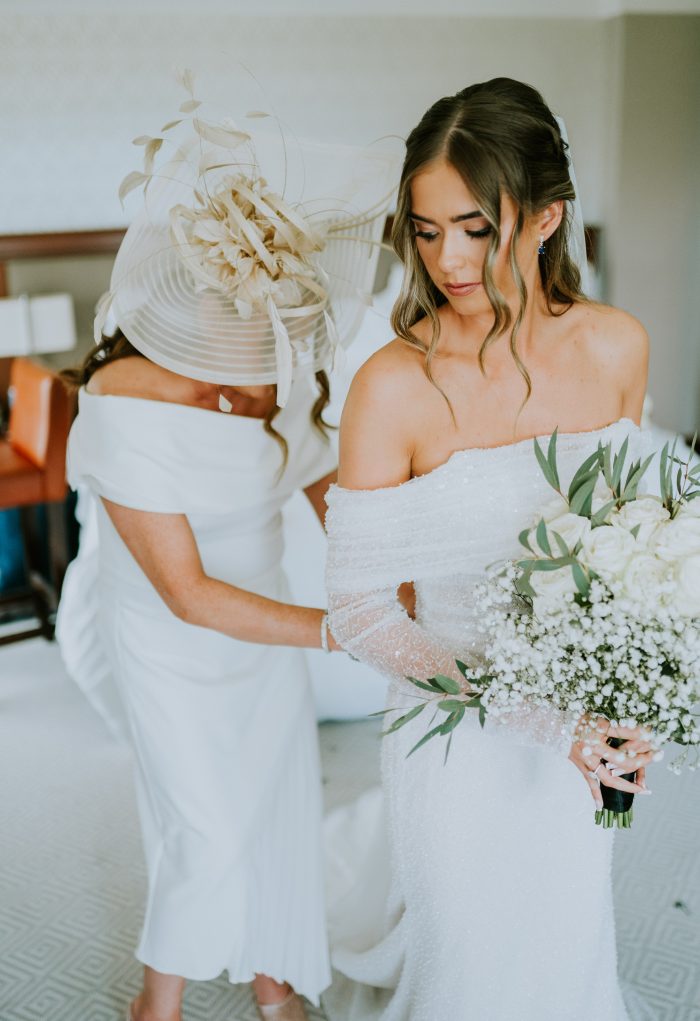 Brides mom zipping up the wedding dress zipper on a bride wearing a long-sleeve wedding gown