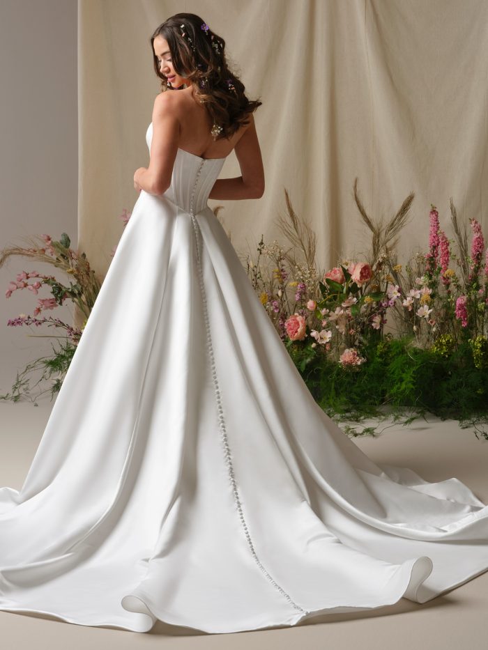 Back view of the Alexia wedding dress showing the structured mock two-piece bodice, button-down detailing, and a full A-line skirt flowing into a long train.