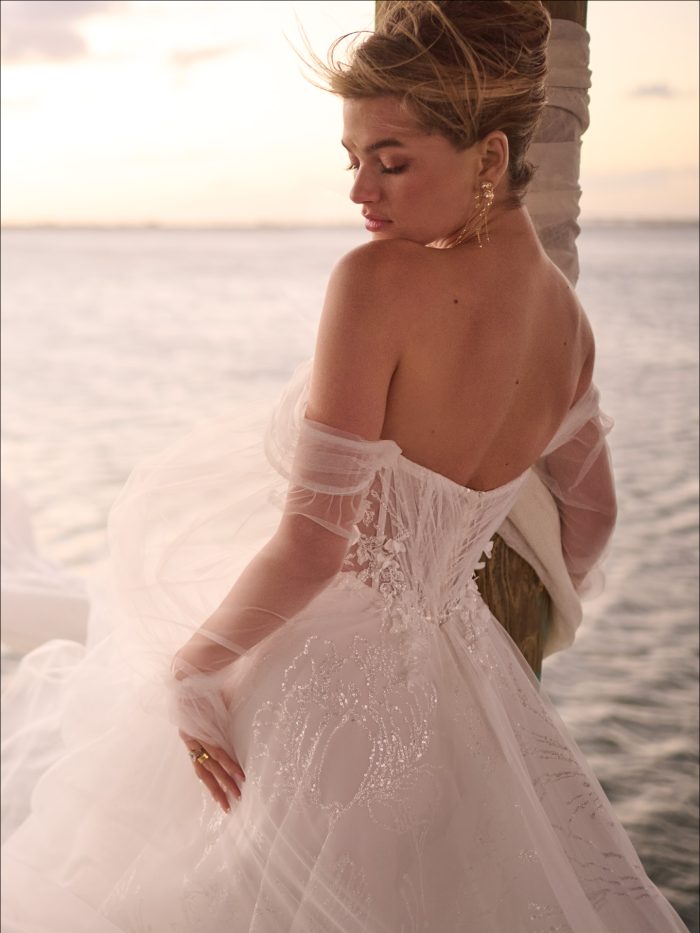 Bride on a beach wearing a glamorous A-line sparkly wedding gown with off-the-shoulder long sleeves