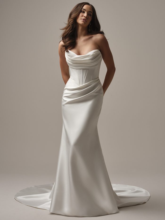 Model wearing the Melissa by Maggie Sottero strapless fit-and-flare wedding dress with a softly draped neckline, corset bodice, smooth satin skirt, and subtle train.