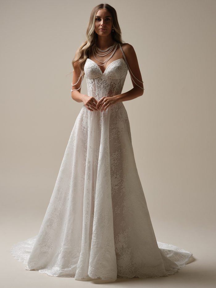 Model wearing the Narissa by Sottero and Midgley A-line wedding dress with a plunging lace bodice, delicate spaghetti straps, and a flowing lace skirt in a studio setting.