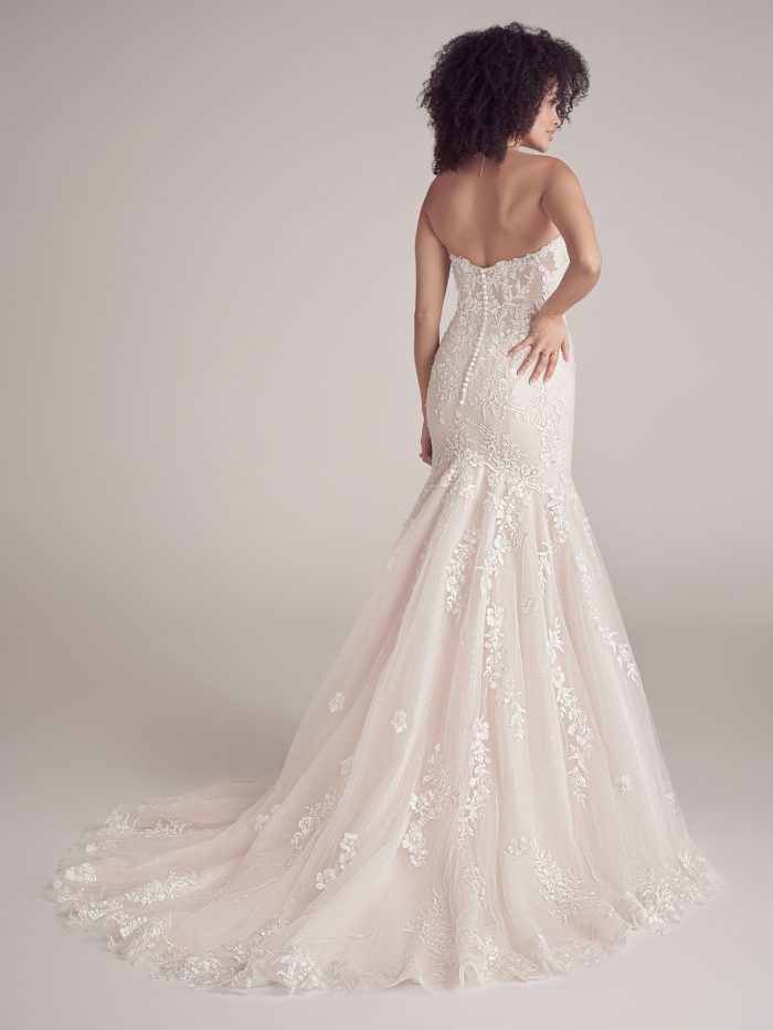 Back view of the Maggie Sottero Lennon bridal gown showing the sheer scoop back, lace detailing, covered button closure, and extended glitter tulle train adorned with floral lace motifs.