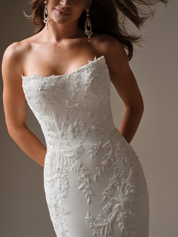 Detail of the Maggie Sottero Thera gown showing the strapless neckline and intricate floral lace appliqués on the fitted bodice.
