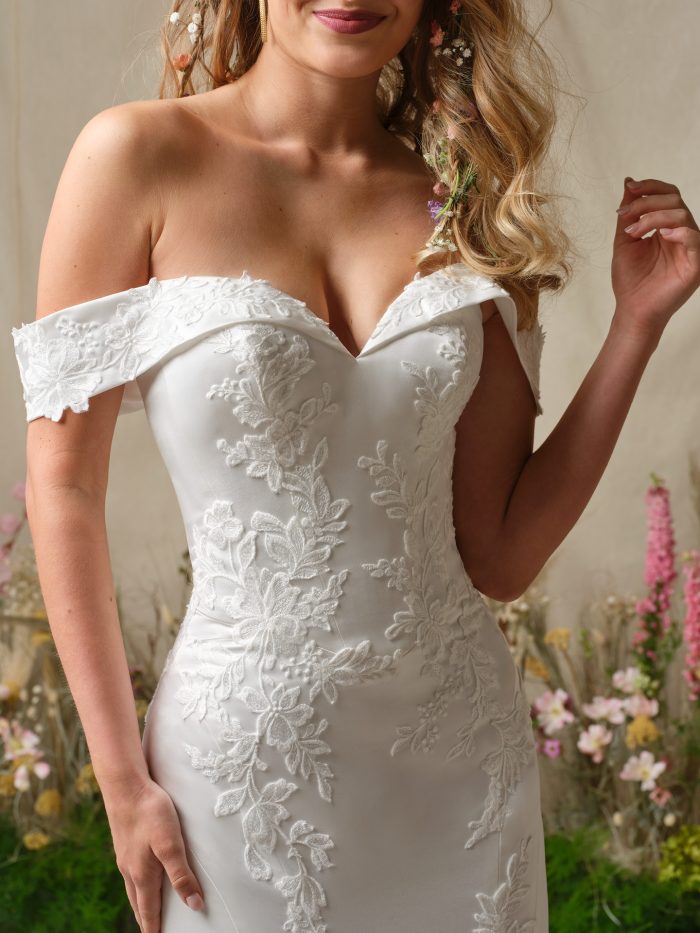 Detail of the Rebecca Ingram Miley gown showing the off-the-shoulder sweetheart neckline with floral lace appliqués along the fitted bodice.