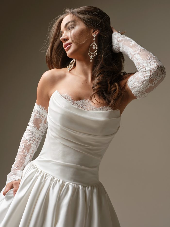 A close-up of the Maggie Sottero Sylvana wedding dress showing the draped satin neckline, lace-trim detail and detachable lace arm sleeves.
