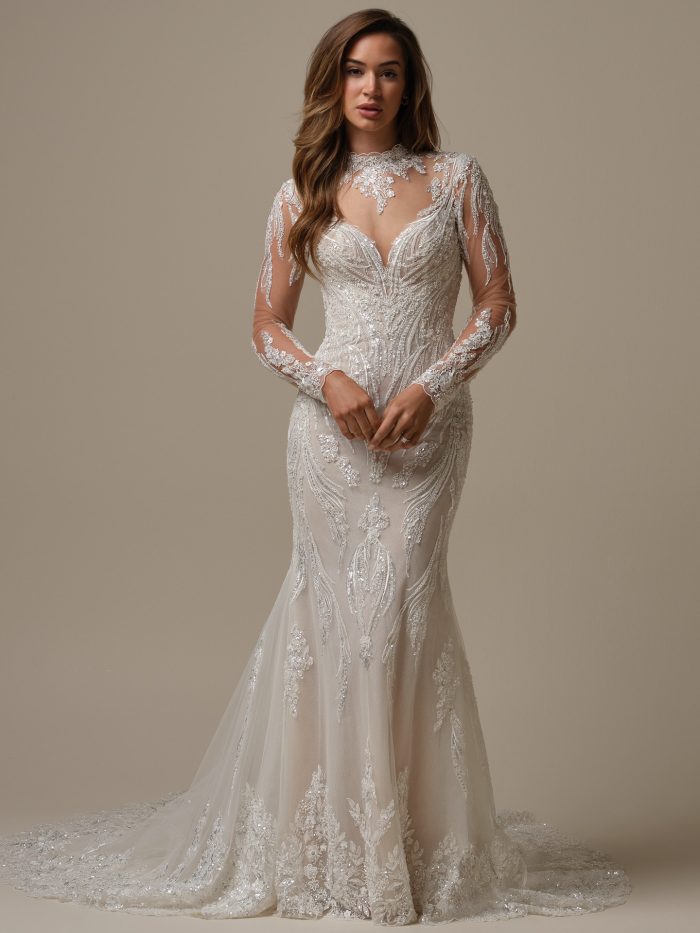 Full-length view of the Torrence sheath wedding dress by Maggie Sottero with long illusion lace sleeves, a sculpted beaded lace silhouette, and a soft train with lace appliqués.