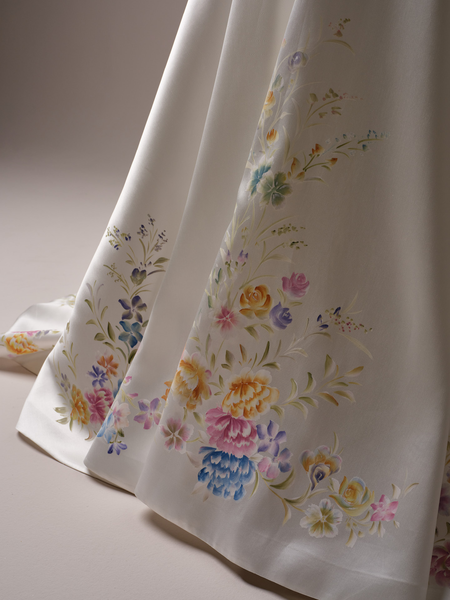 Close-up of satin wedding dress skirt with delicate hand-painted floral motifs in soft multicolor tones