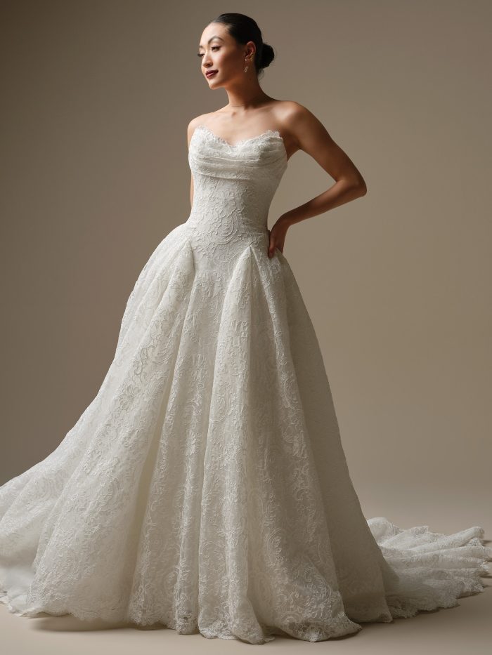 A model wearing the Sottero and Midgley Tamar wedding dress, featuring unembellished allover lace, an asymmetrically draped strapless sweetheart bodice and a full A-line skirt.